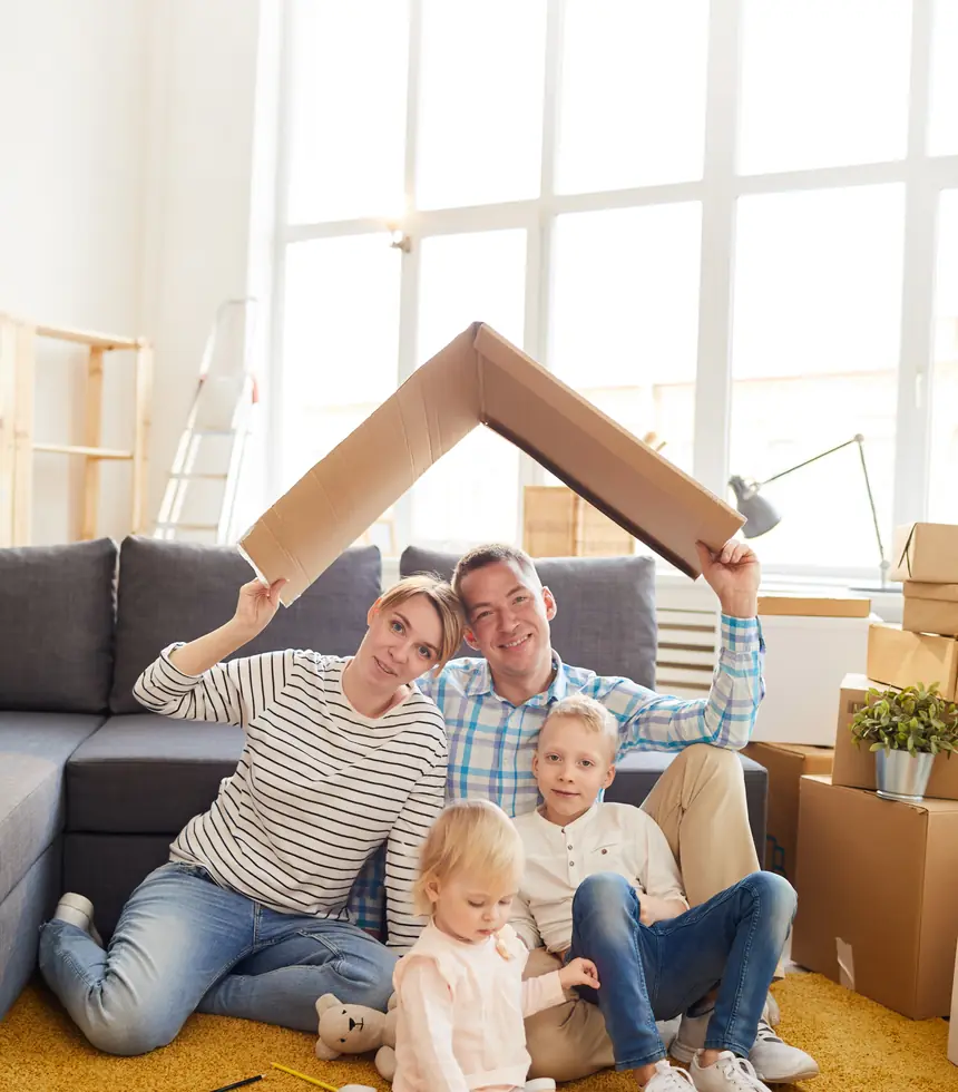 Une famille assise au milieu des cartons d'un emménagement, un toit de carton tenu à bout de bras — les 3 paliers à passer avant d'hypothéquer sa maison