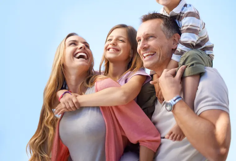 Une famille de quatre, serrée les uns contre les autres, rit sous un ciel dégagé — le regroupement de crédits sans hypothèque